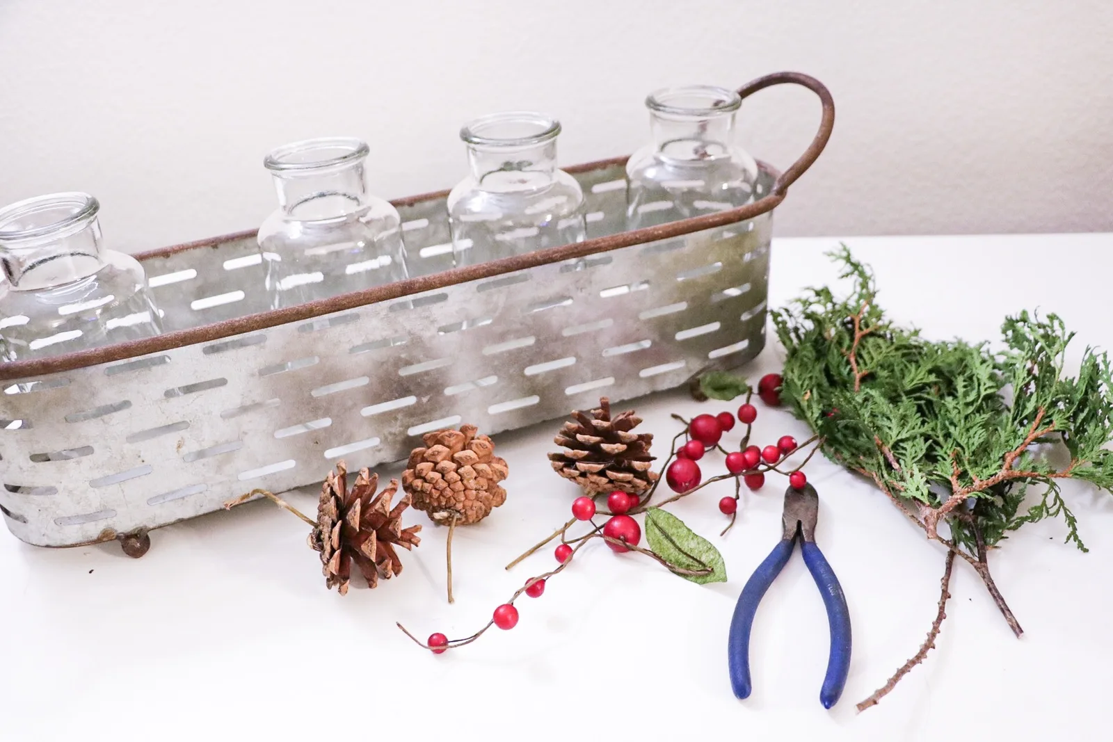 Fresh cedar, holly berries and pinecones arranged in a multi vase centerpiece on a table