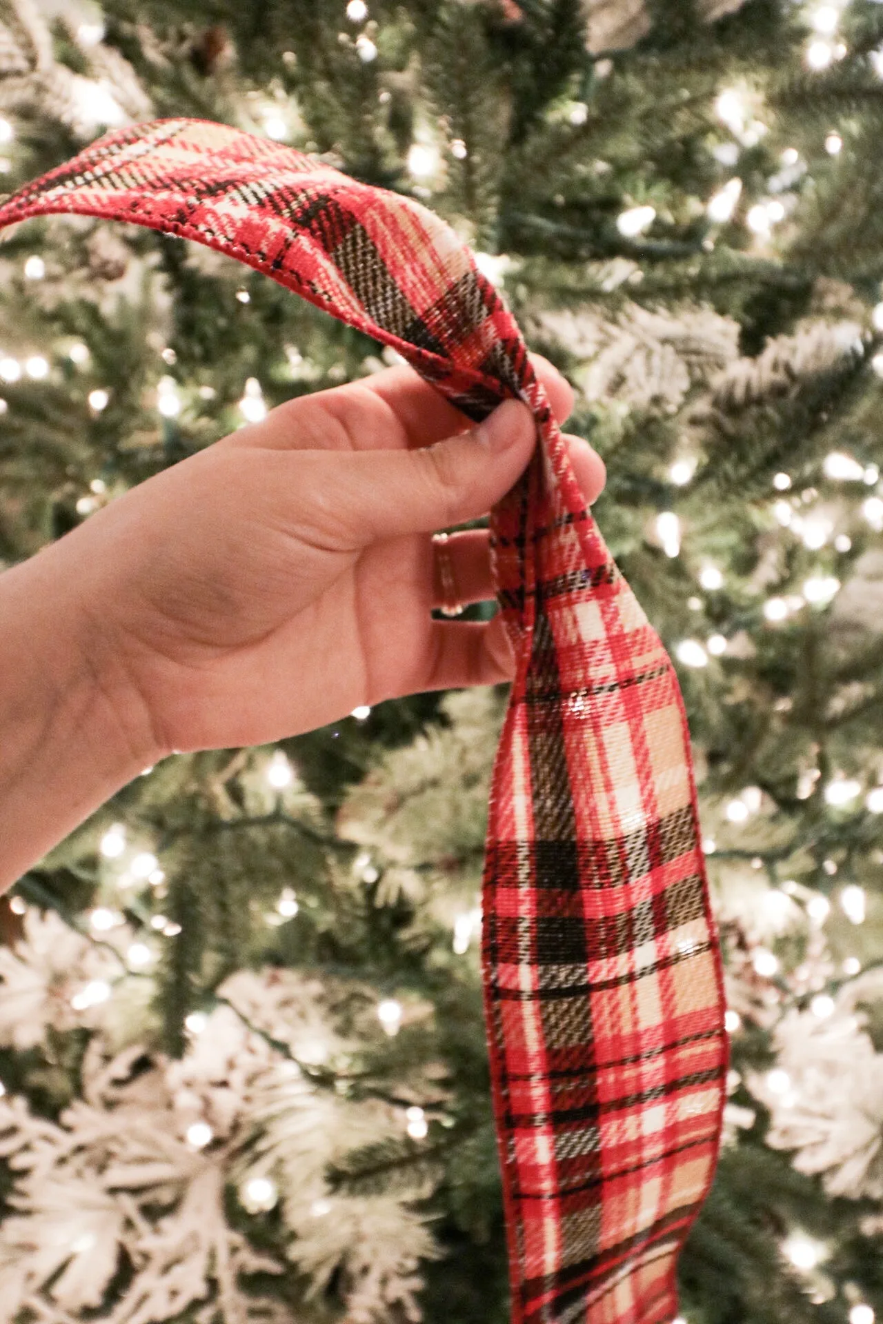 Hands pinching wired Christmas ribbon and tucking it into the branches of a decorated tree