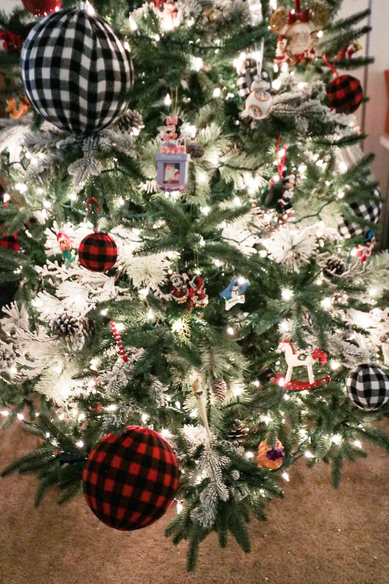 A lit artificial Christmas tree decorated with buffalo check baubles, every string working
