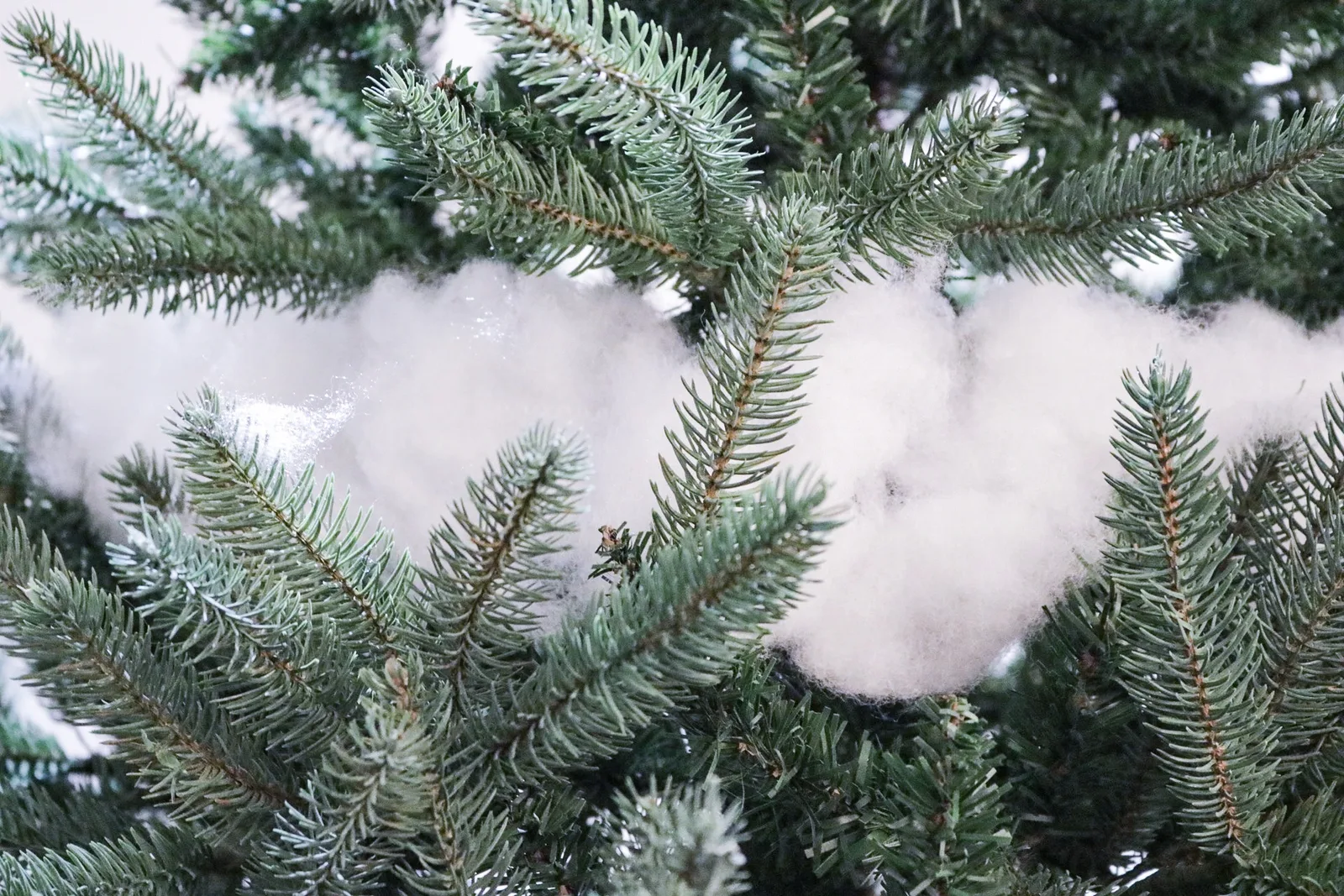 Close-up of an artificial tree branch with white fibre fill tucked between the tips to fake snow and fill gaps